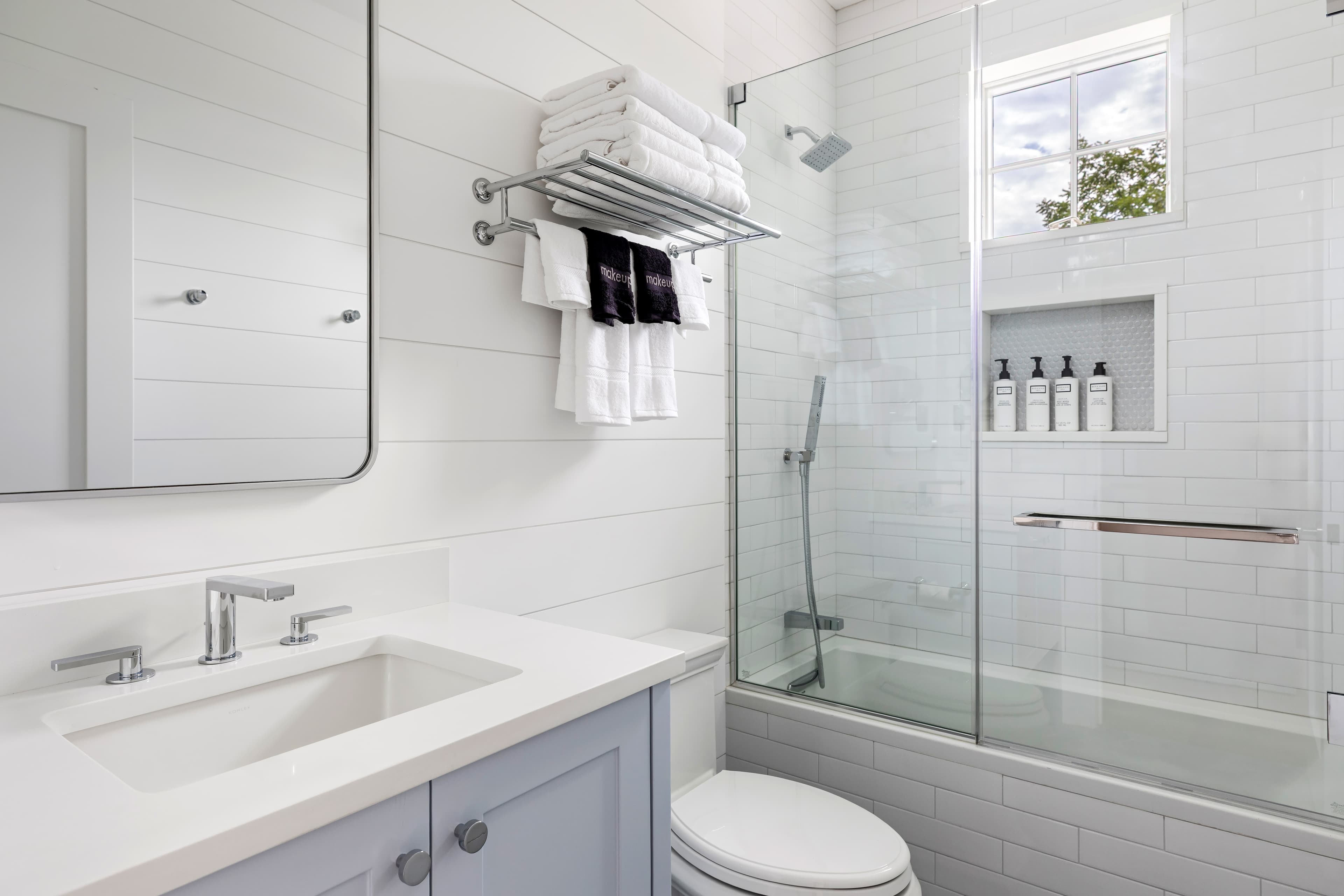 A modern bathroom featuring a glass shower, white tiles, and a stylish light blue vanity.