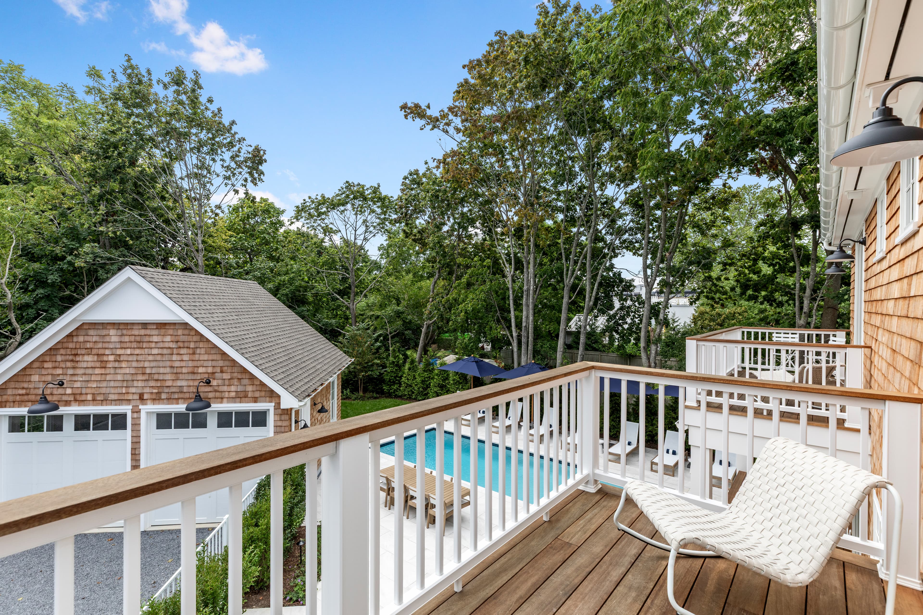 A view from a balcony overlooking a pool surrounded by trees and a neighboring house.