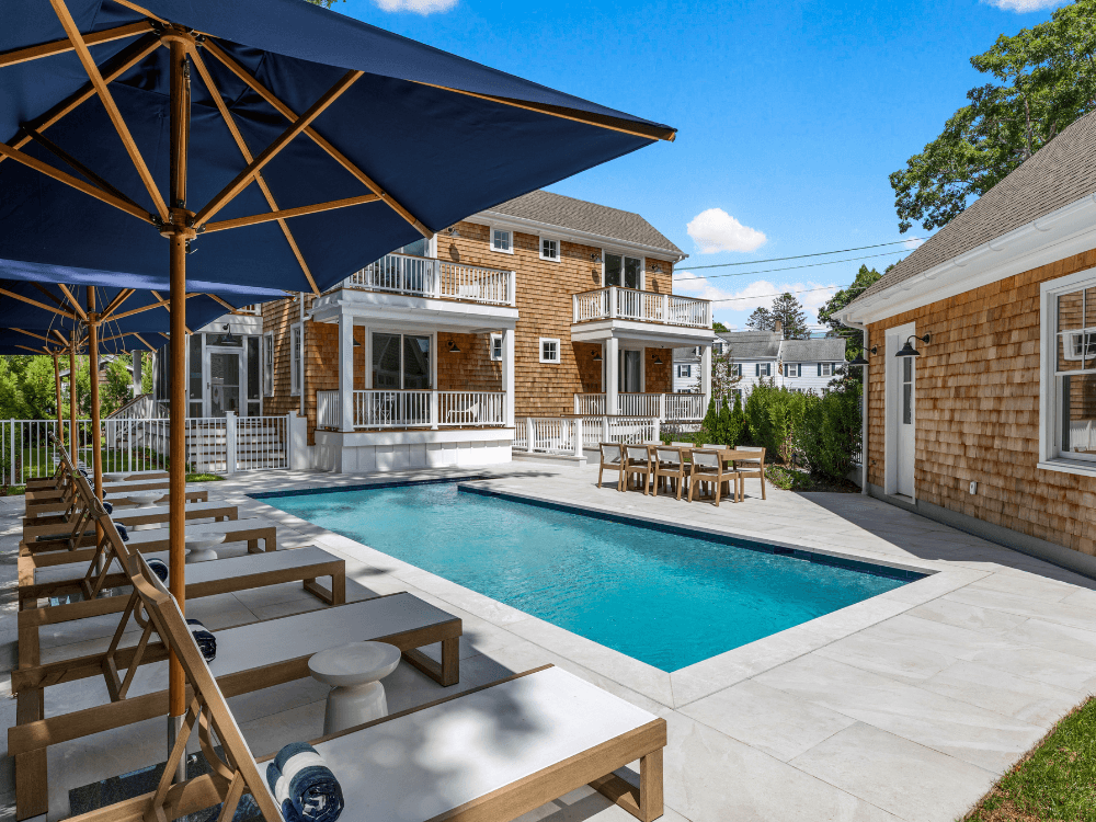 A stylish backyard features a swimming pool surrounded by lounge chairs and umbrellas.