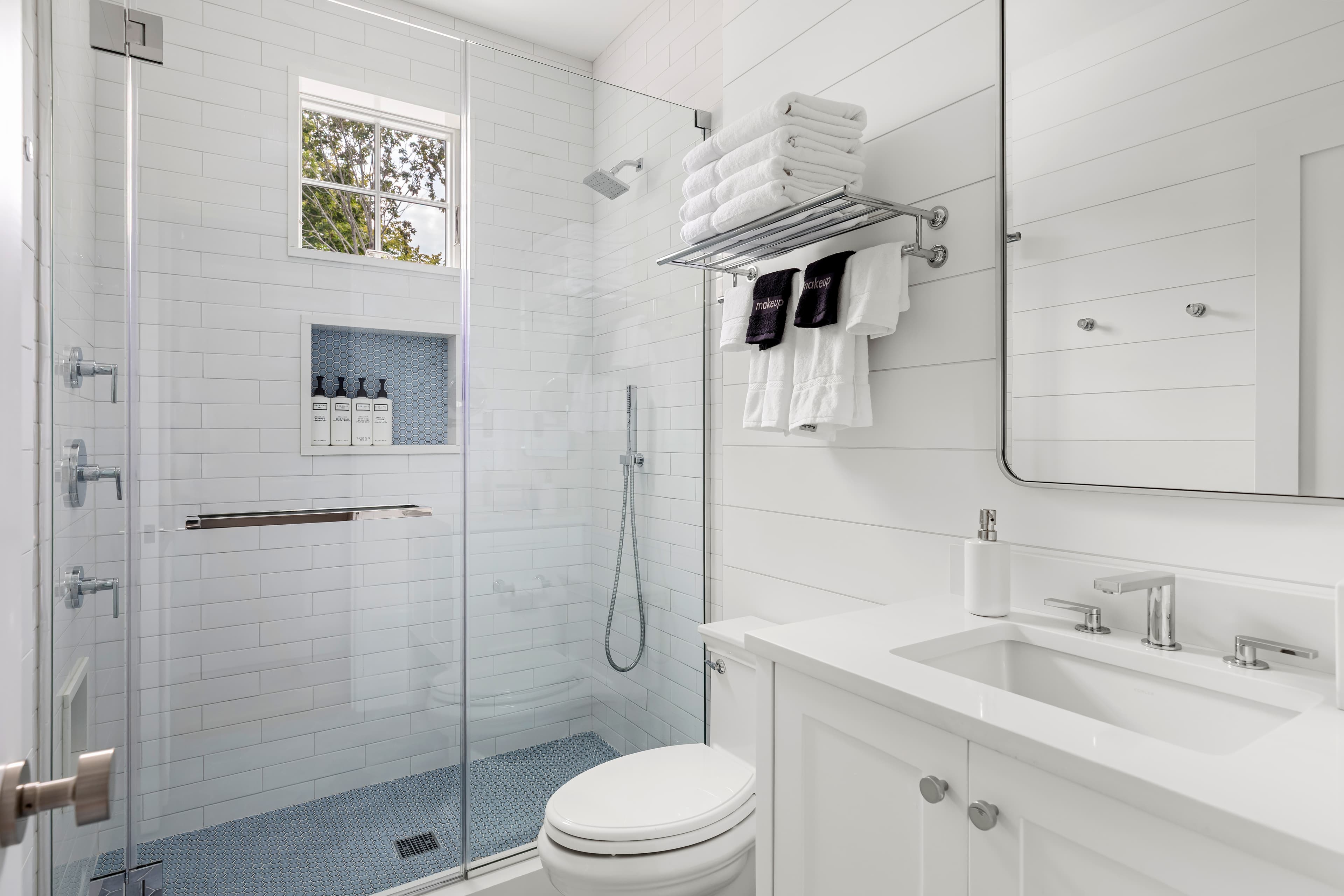 A modern bathroom featuring a glass shower, white tiles, and neatly arranged towels.