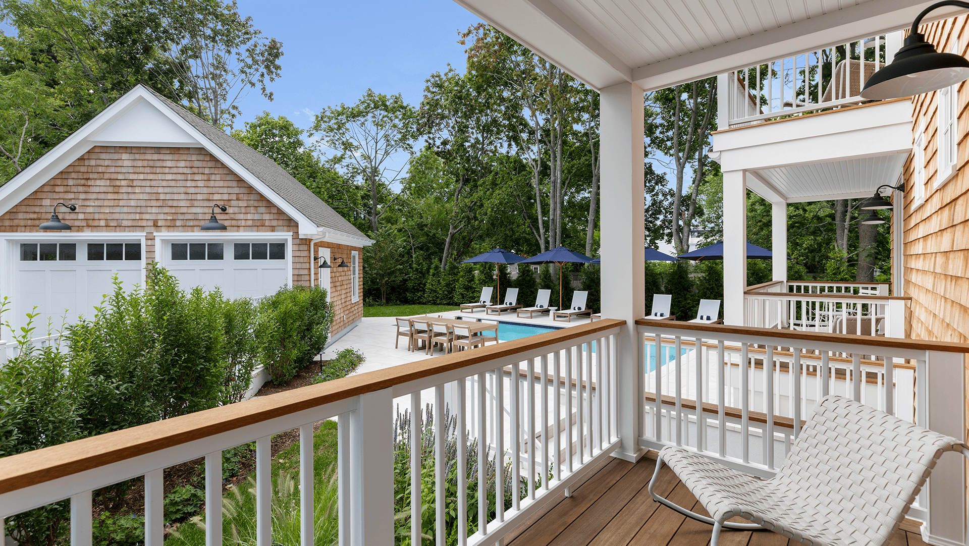 A view from a balcony overlooking a pool area surrounded by trees and a garage.