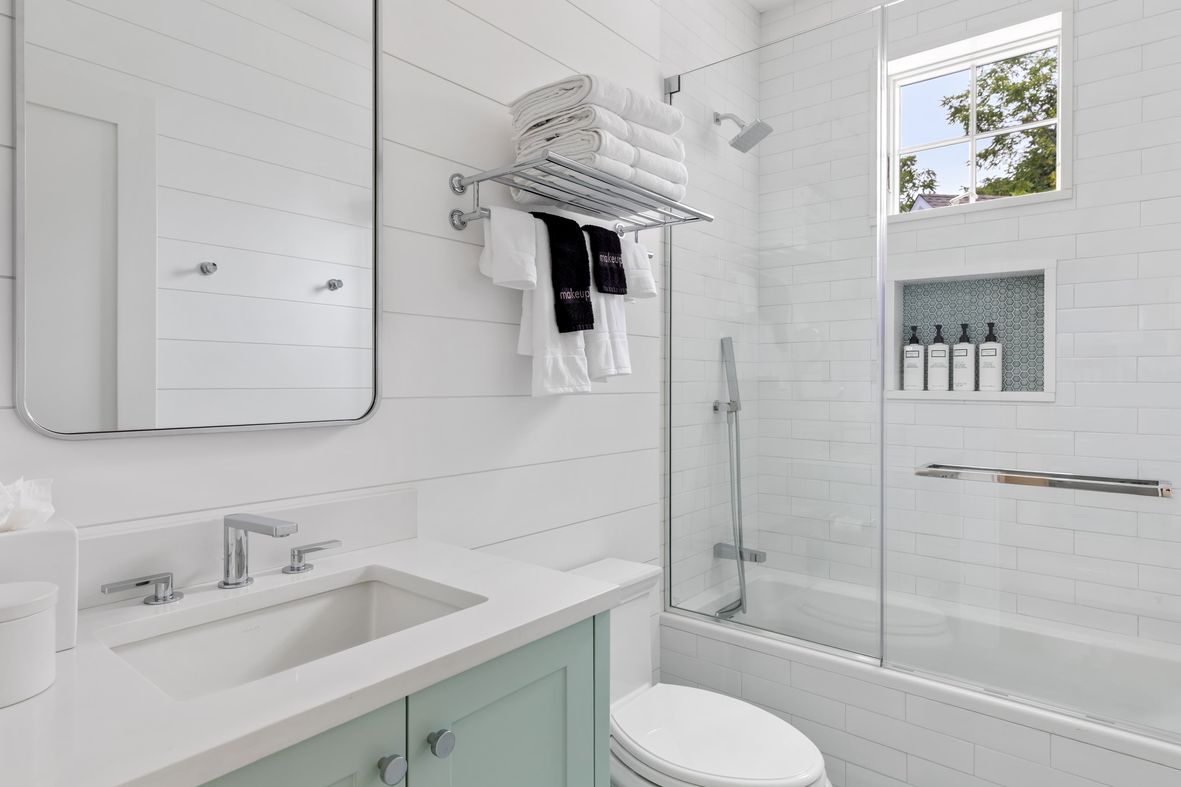 Modern bathroom featuring a glass shower, white tiles, a large mirror, and neatly arranged towels.