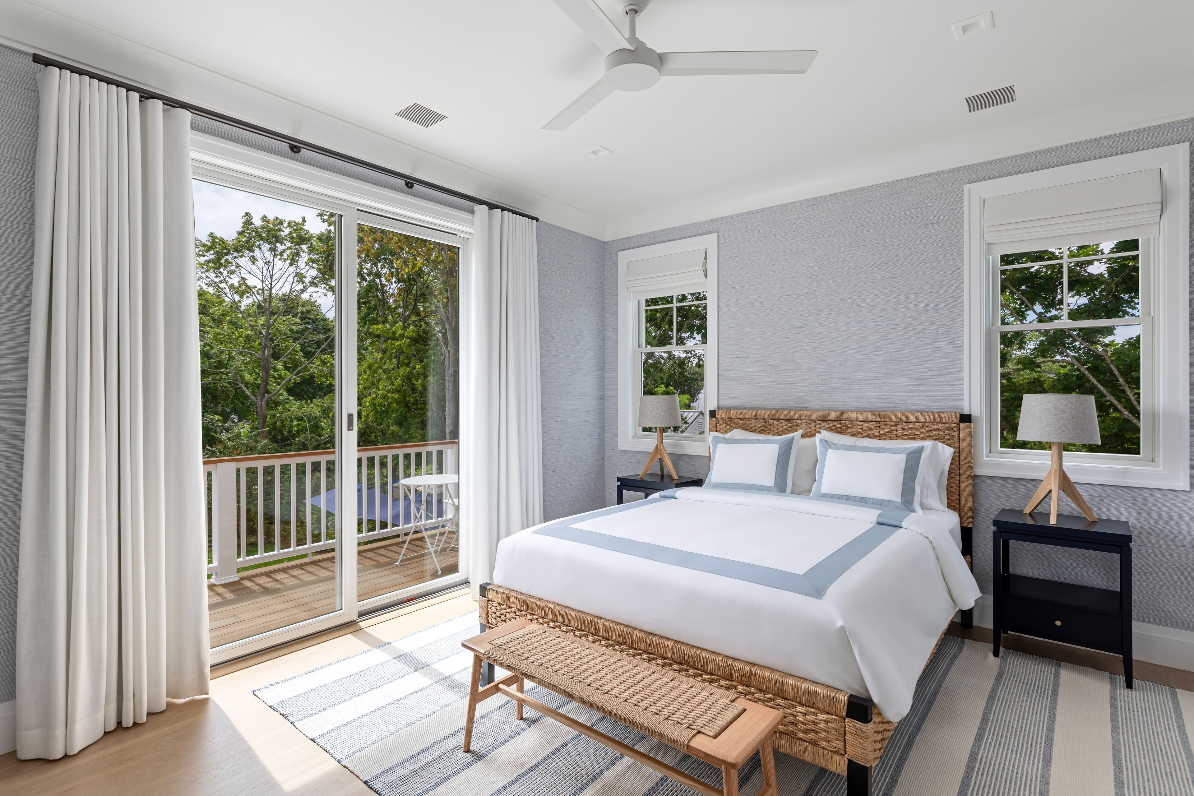 A bright, modern bedroom featuring a woven bed, two nightstands, and large windows opening to a balcony.