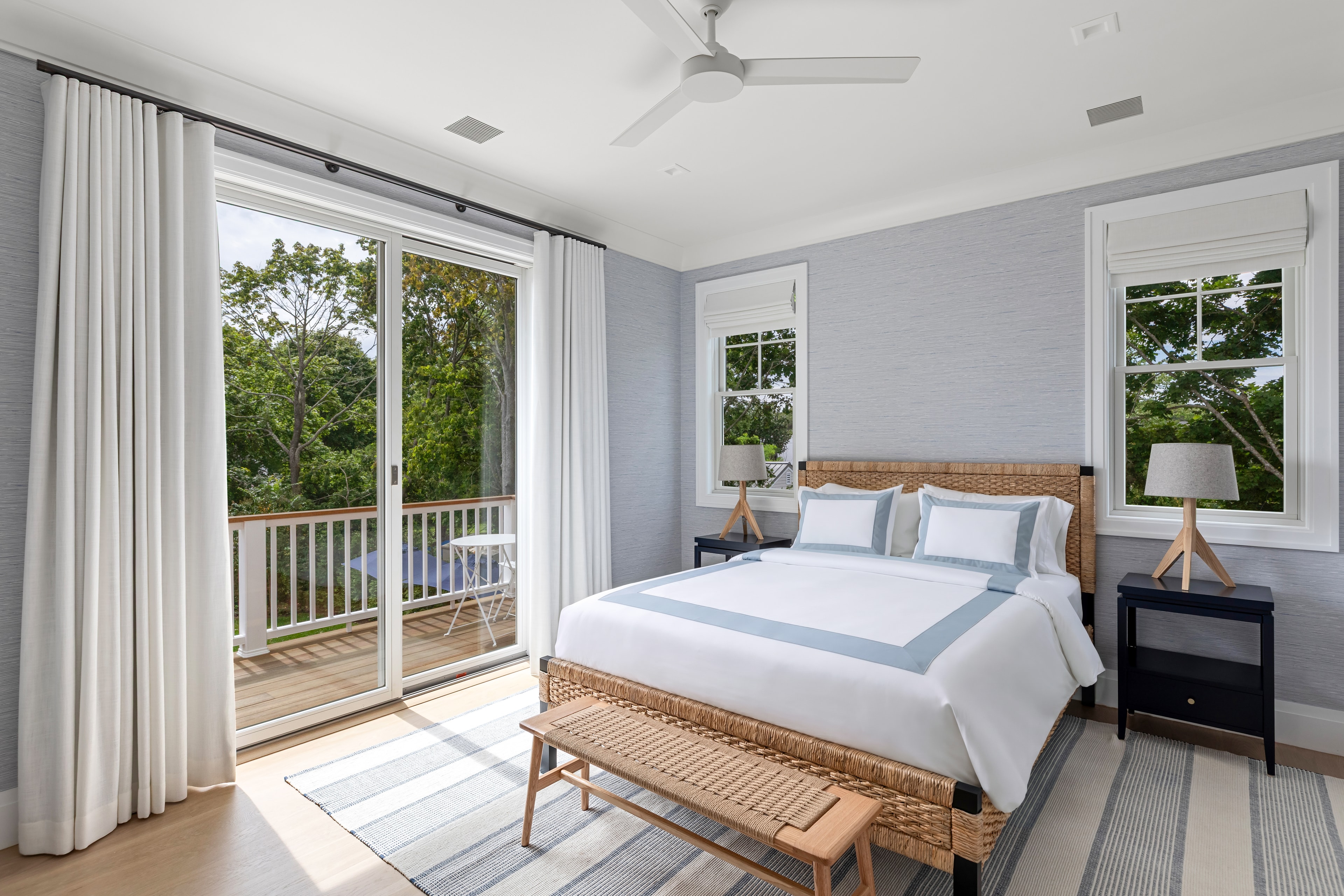 A bright, modern bedroom featuring a woven bed, two nightstands, and large windows opening to a balcony.