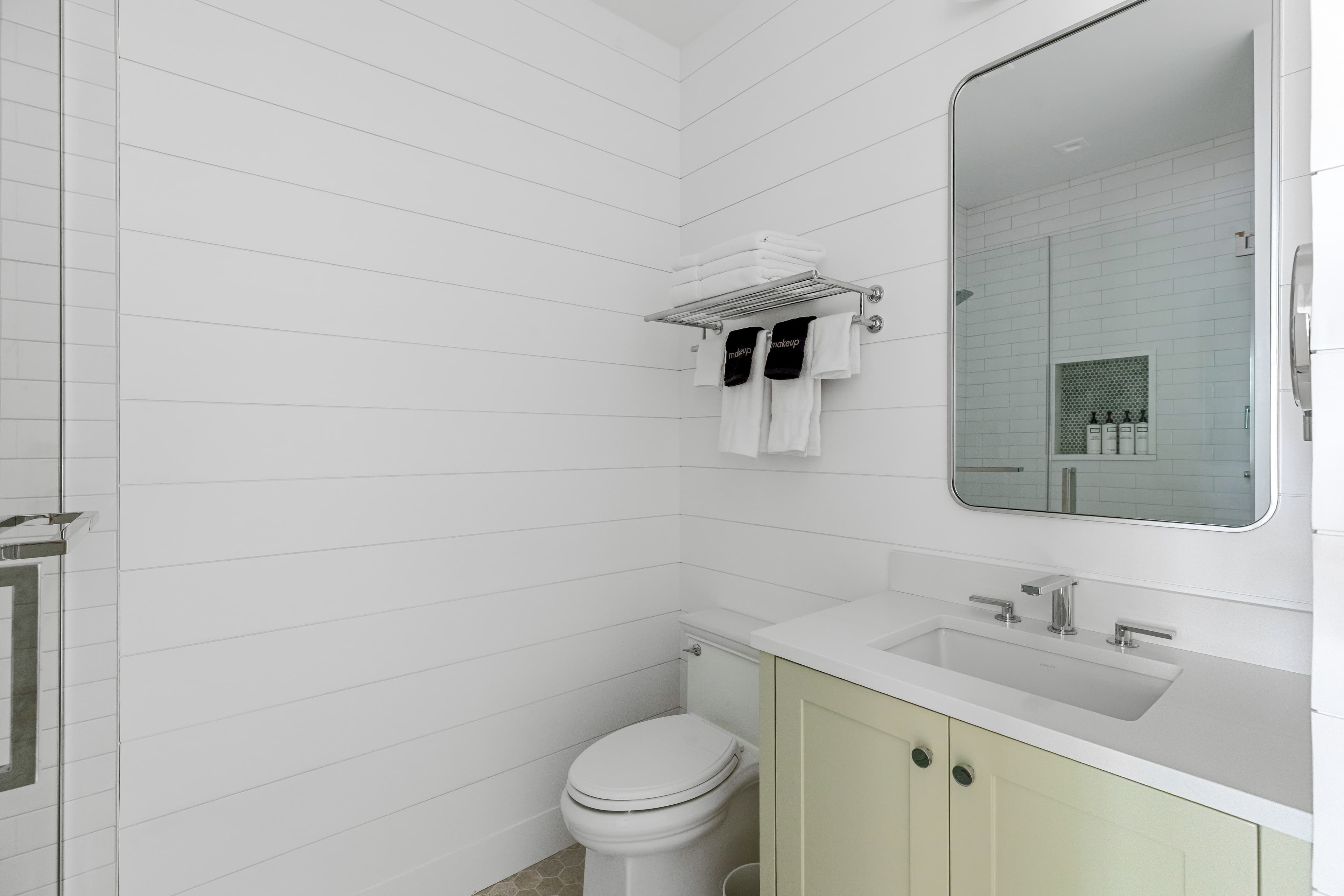 Modern bathroom with white shiplap walls, a mirror, sink, and a shower.