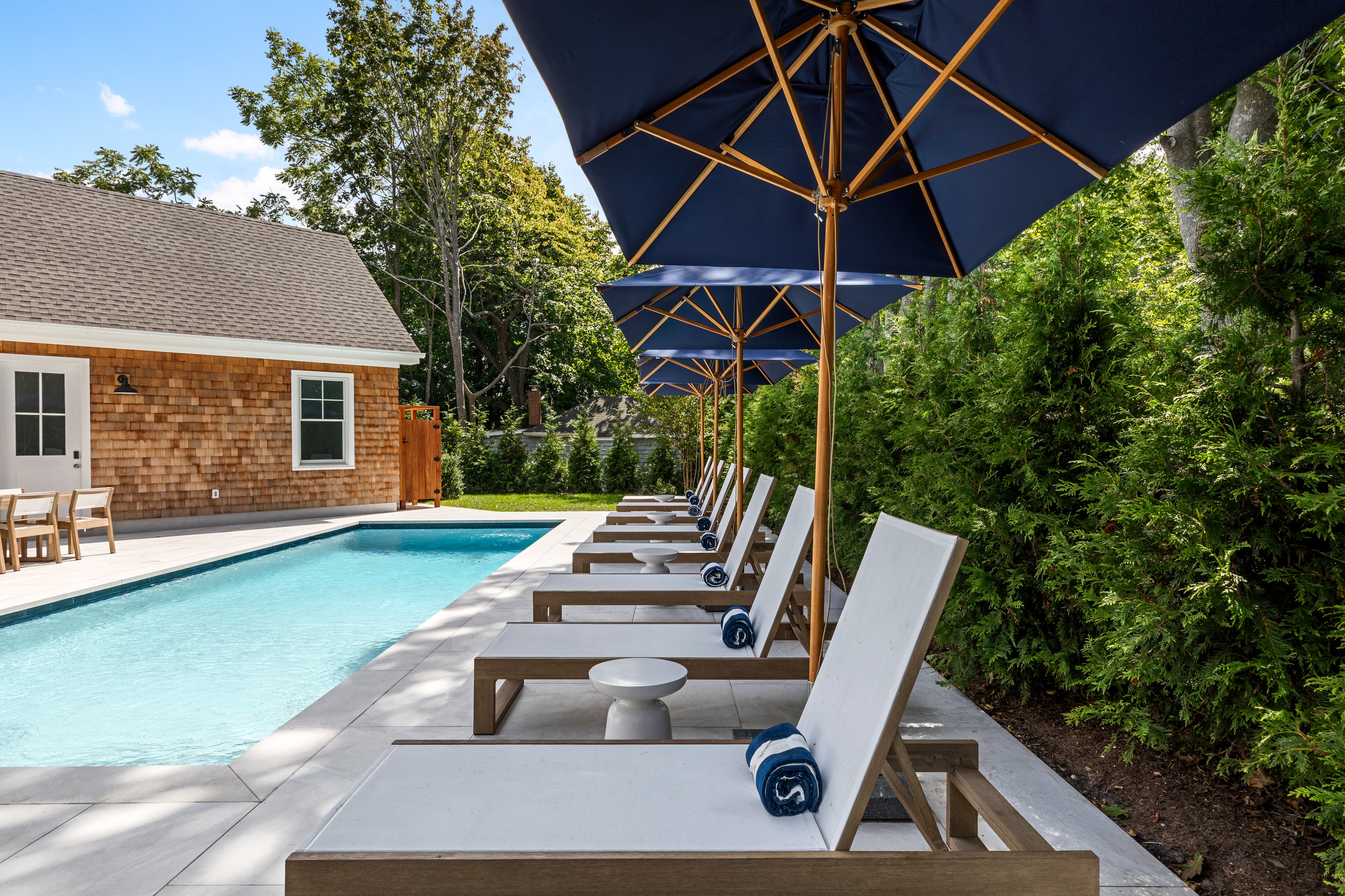 A sunny poolside area featuring lounge chairs and umbrellas beside a swimming pool.