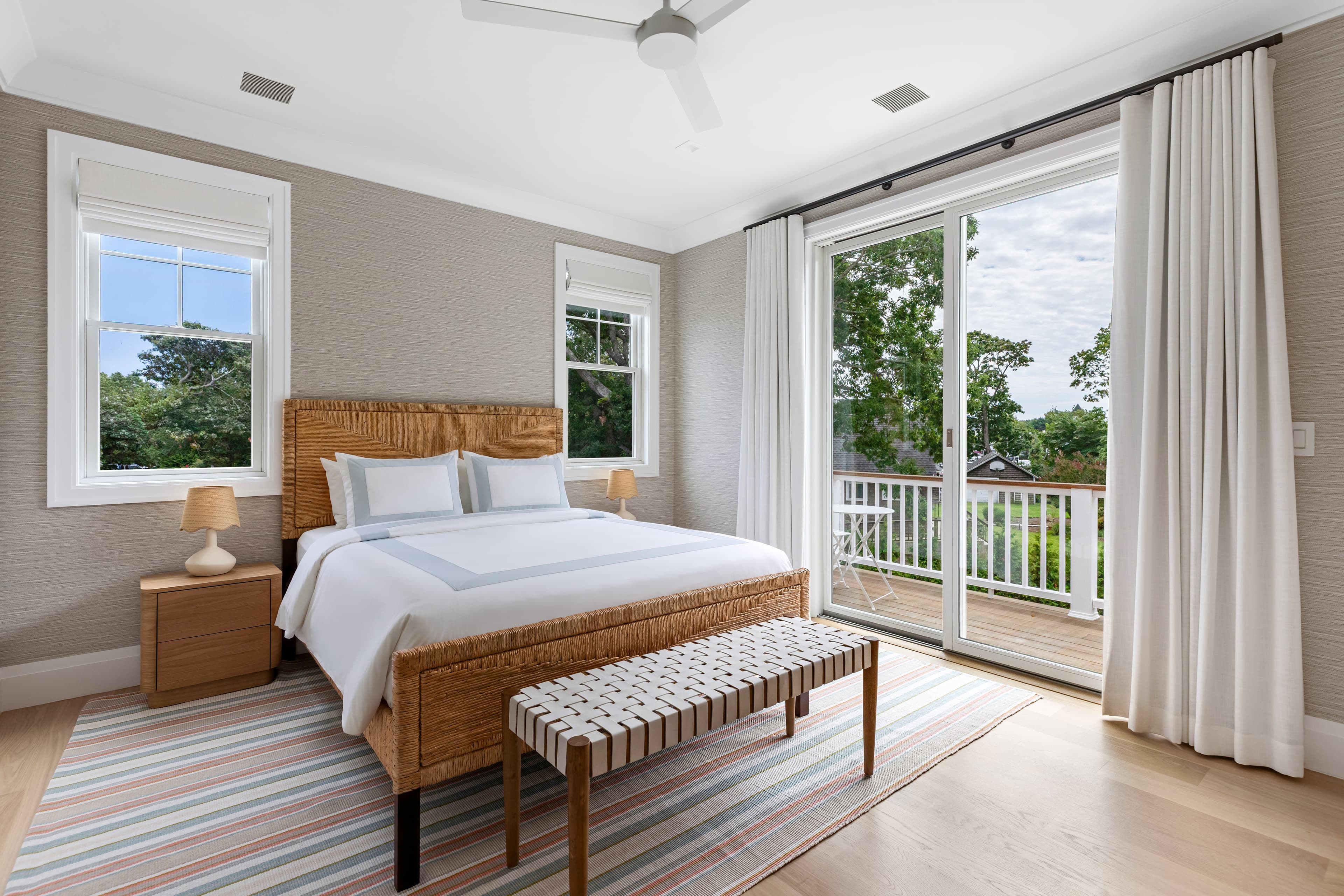 A spacious, modern bedroom featuring a wicker bed, striped rug, and balcony access.