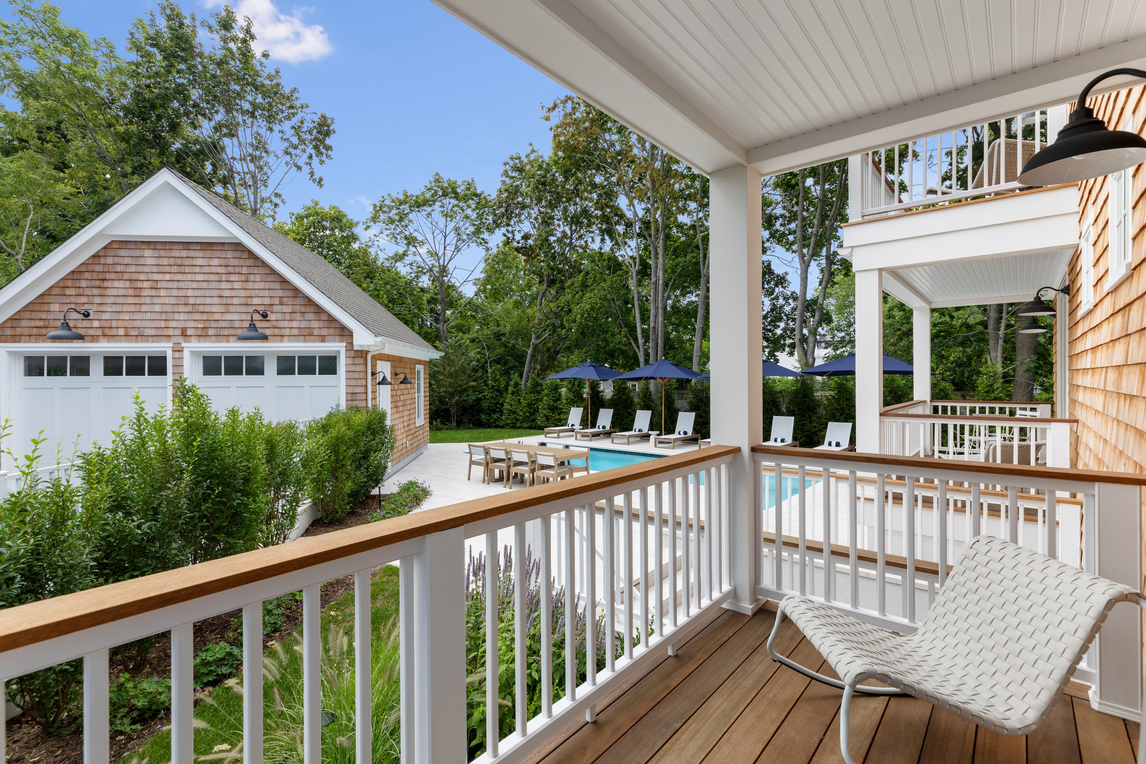 View from a porch overlooking a pool area with lounge chairs and a garage in a lush, green setting.