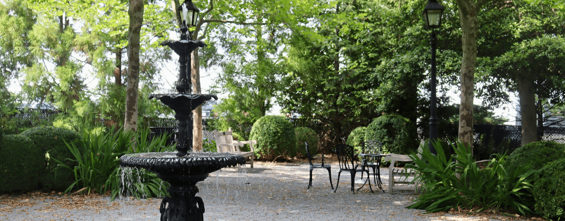 A tranquil garden featuring a black fountain, surrounded by lush greenery and seating areas.