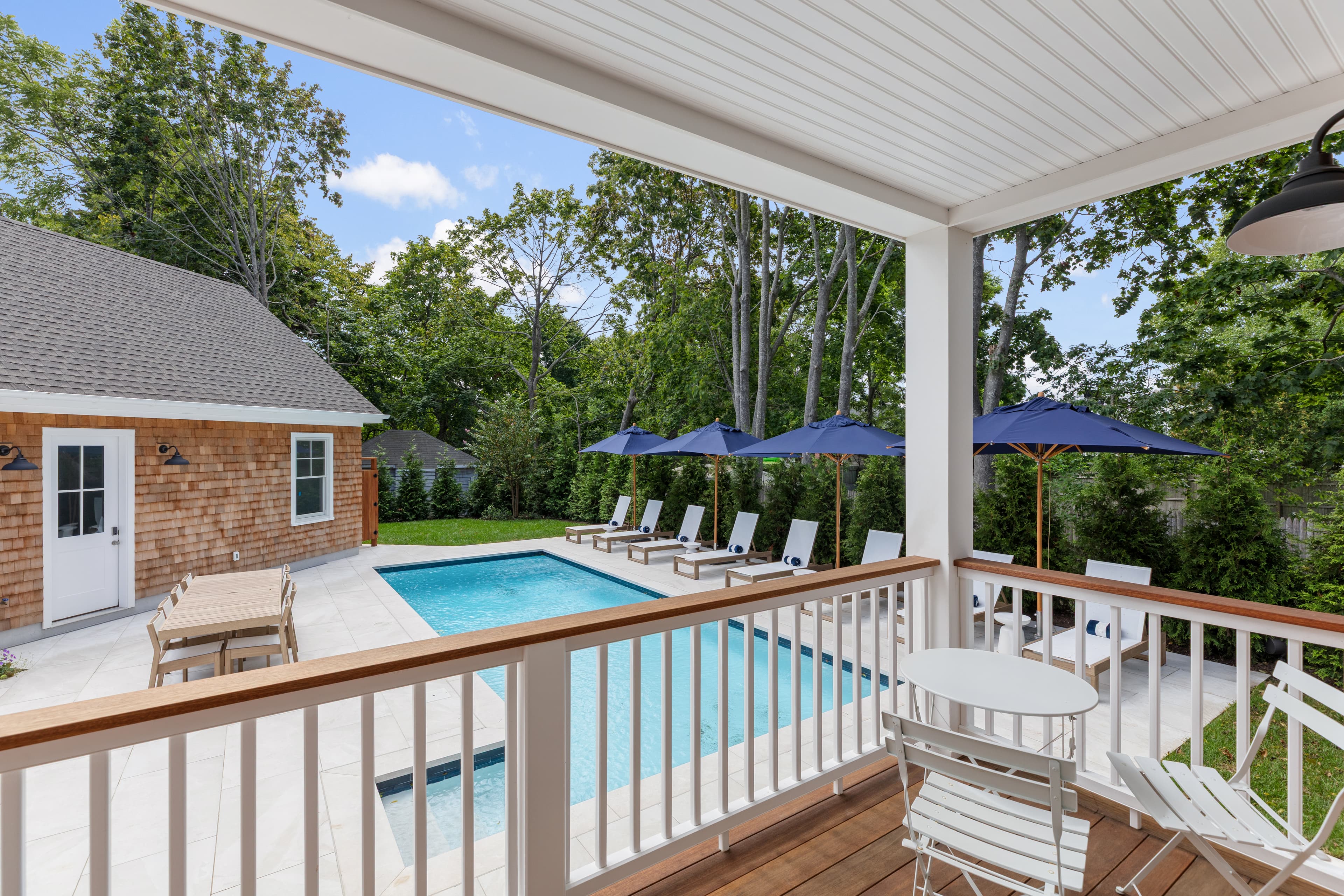 A modern outdoor pool area with loungers and umbrellas, viewed from a covered porch.